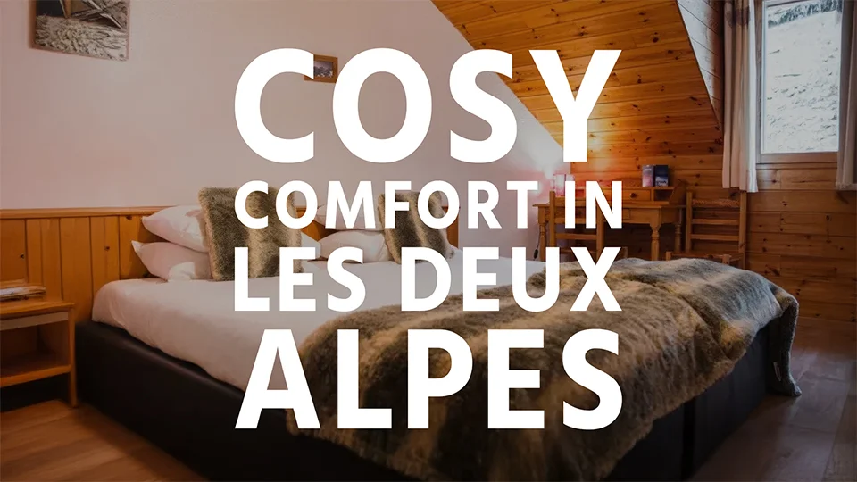 A double bed with cosy bed coverings in a ski chalet in Les Deux Alpes with text overlay 'Cosy comfort in Les Deux Alpes'