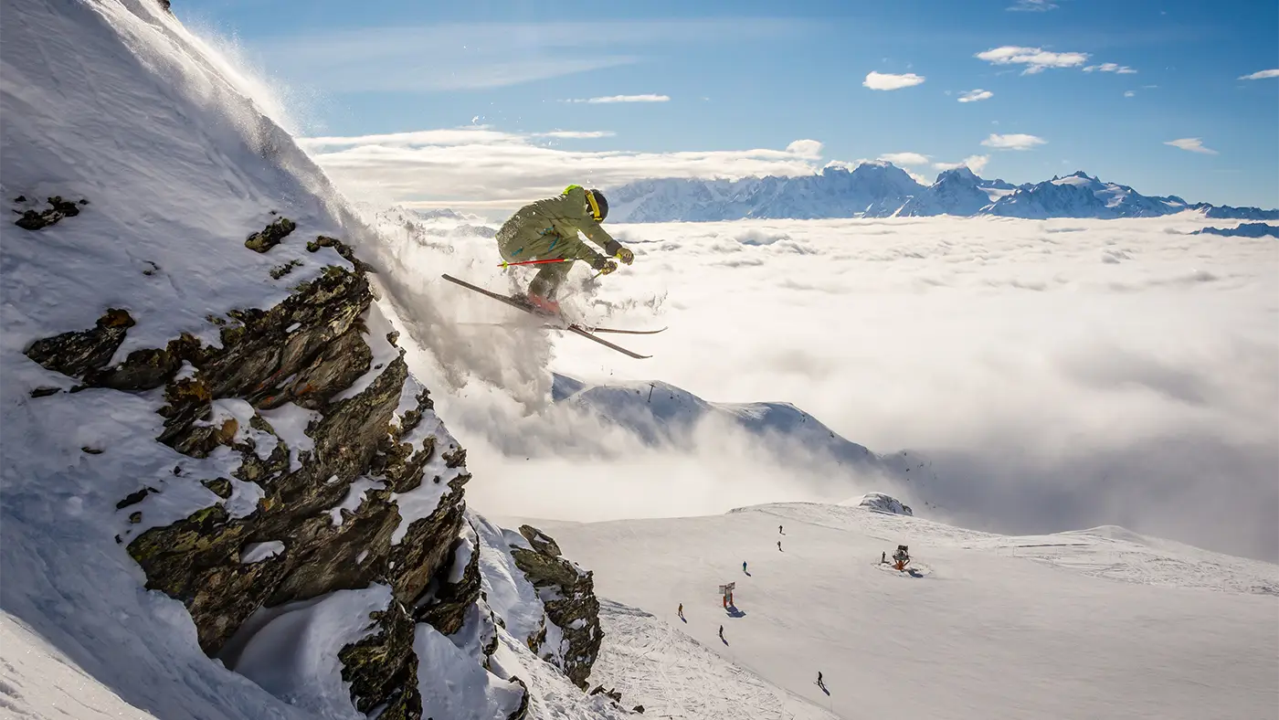 An off-piste skier flies of the edge of a rock at high altitude