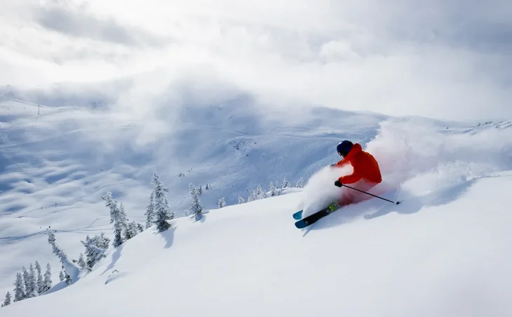 A skier skiing down the pristine powder covered expanses of Whistler, Canada. A blanket of snow covers the whole epic landscape, making Whistler an amazing location for ski holidays in Canada
