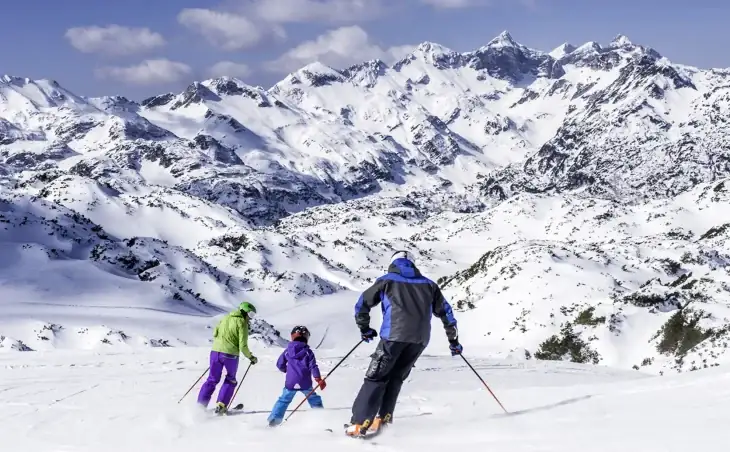 A family of three on a green piste on ski holiday in France. In the background we can see the Alps