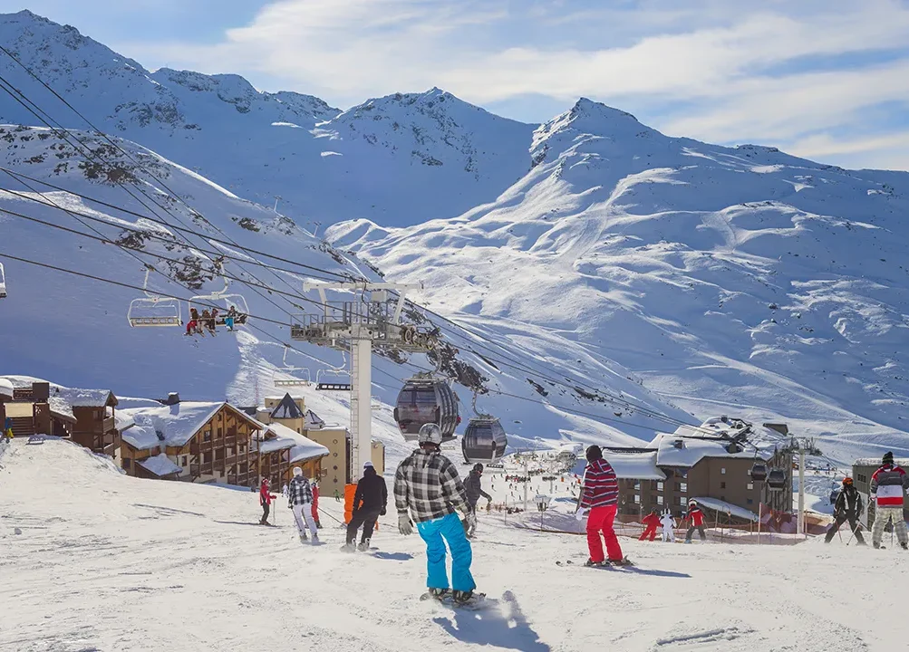 Val Thorens Ski Holidays. Skiers descending the slopes of Val Thorens on a bright sunny day. Chair lifts climb and carry skiers in the mid distance