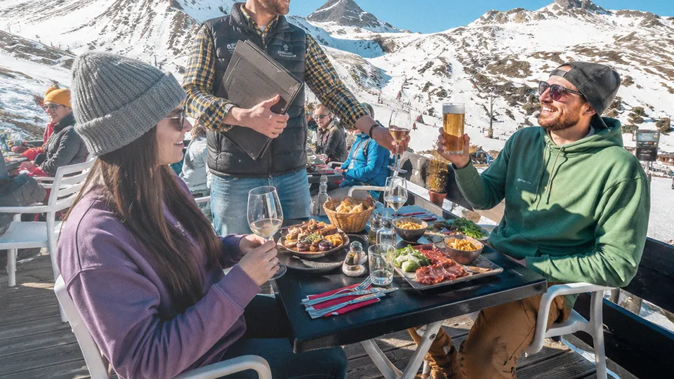 Friends enjoying après-ski dining on a sunny mountain terrace during April ski holidays.