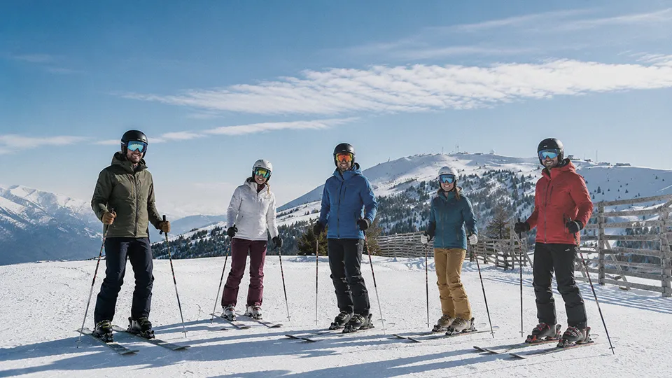 Group of friends skiing on sunny alpine slopes during February ski holidays.