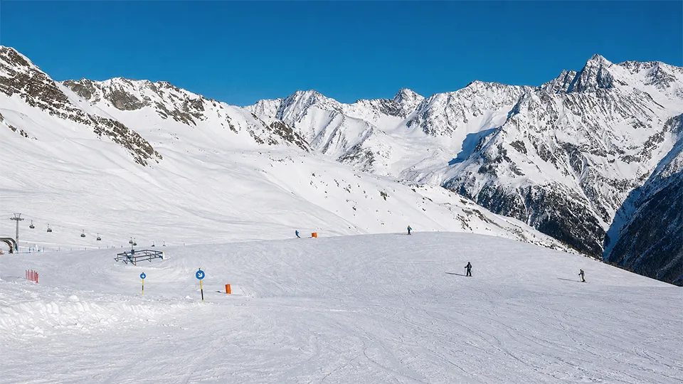 Sunlit ski slope in the Alps with panoramic snow-covered mountains and clear blue skies during a January ski holiday.