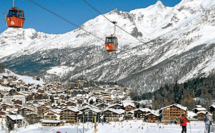 Red cable cars above skiers on the pistes in Saas Fee, Switzerland.